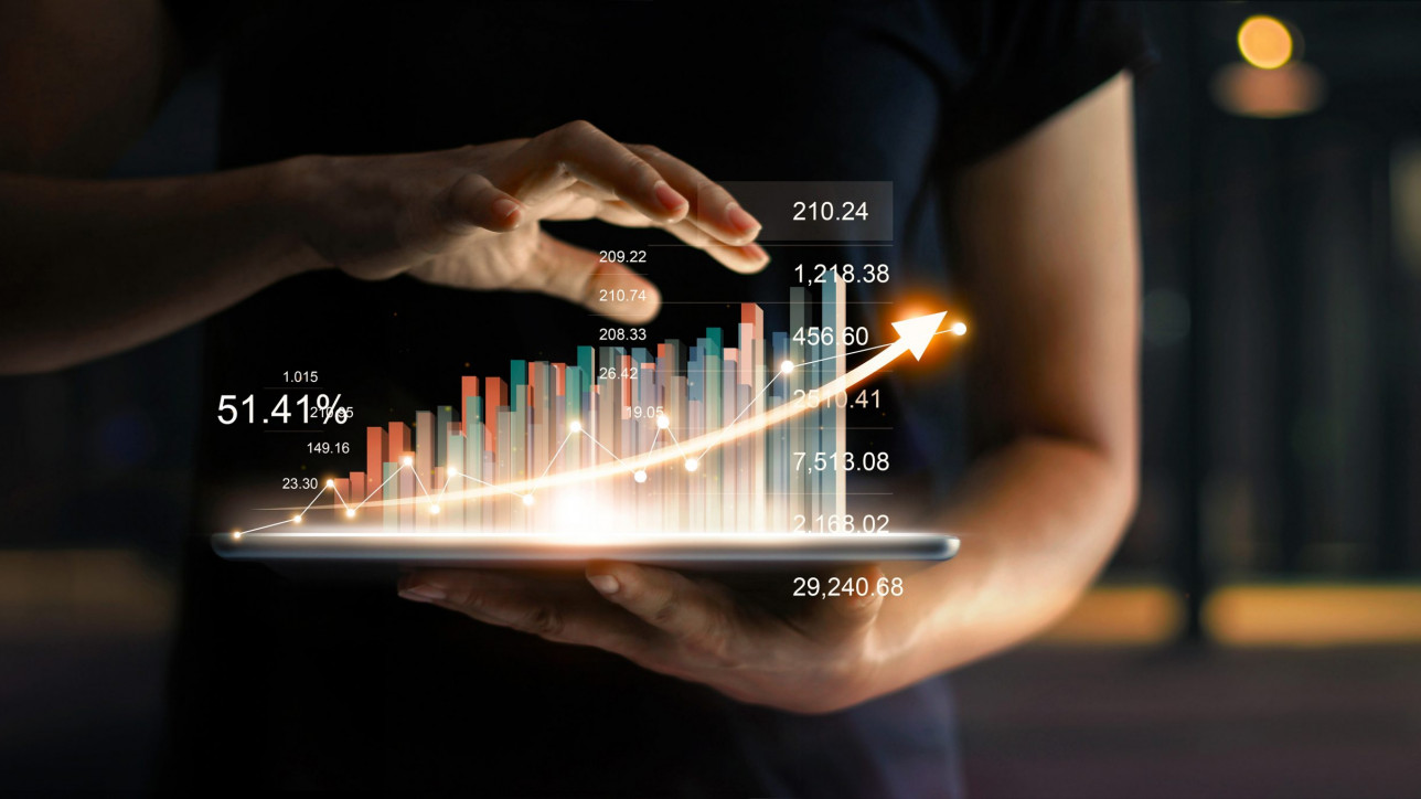 businessman holding tablet and showing a growing virtual hologram of statistics, graph and chart with arrow up on dark background. Stock market. Business growth, planing and strategy concept.